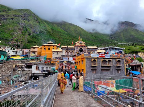 Vibrant view of Badrinath Temple surrounded by lush mountains and visitors crossing a bridge.
